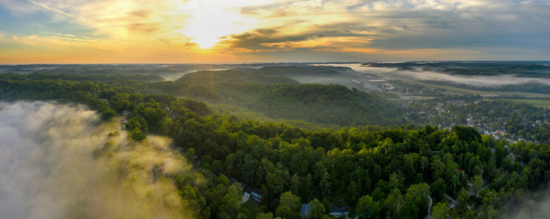 Aerial view of the rolling hills surrounding Athens, Ohio, covered in trees and fog during sunrise.
