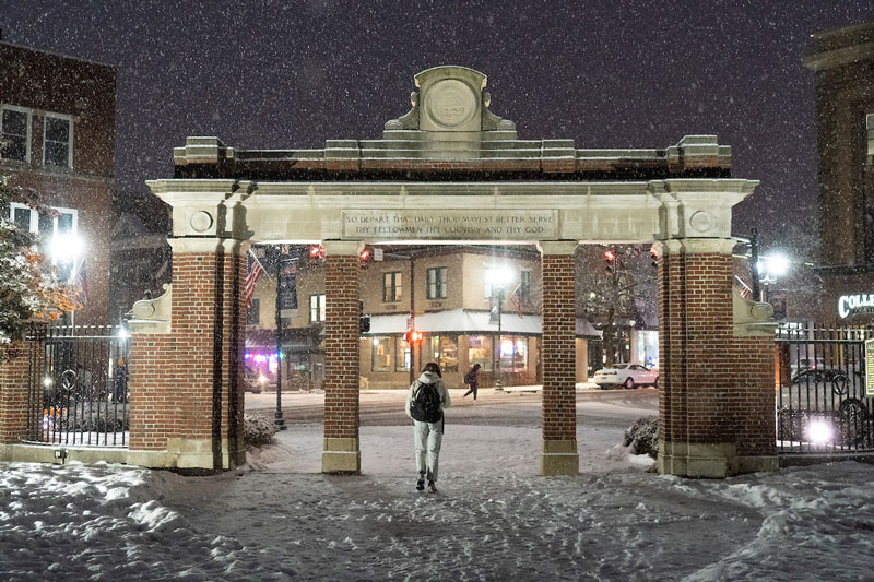 A student walks through the brick Alumni Gateway on College Green.