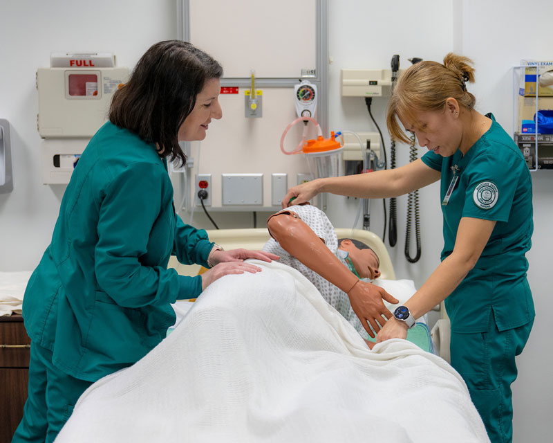 Two nursing students perform a procedure on a medical manikin.