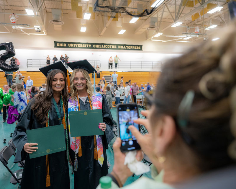 Two students pose with their diplomas while wearing their caps and gowns after graduating.