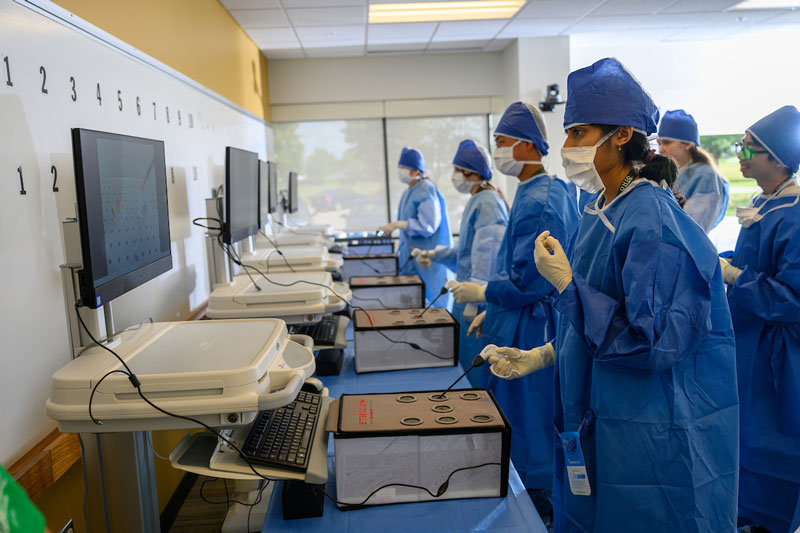 Medical students wear scrubs and PPE during a practice procedure.