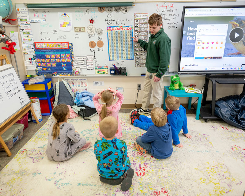 A college student studying education teaches a classroom of children.