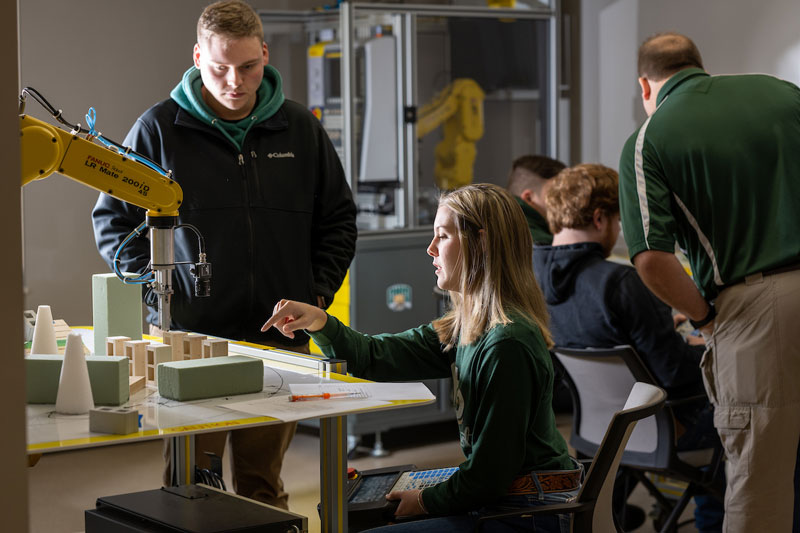 Two students work with engineering machinery in a classroom.