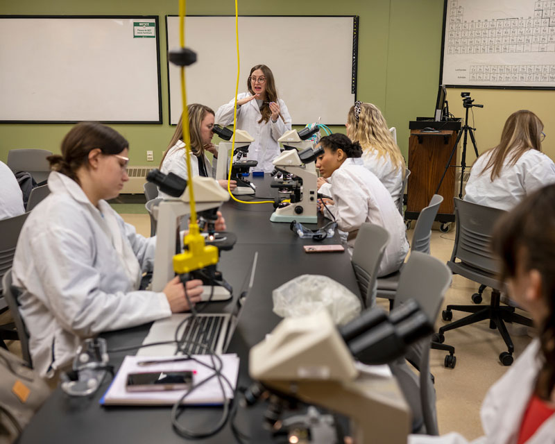 Several students examine microscopes in a classroom on the OHIO Southern campus.