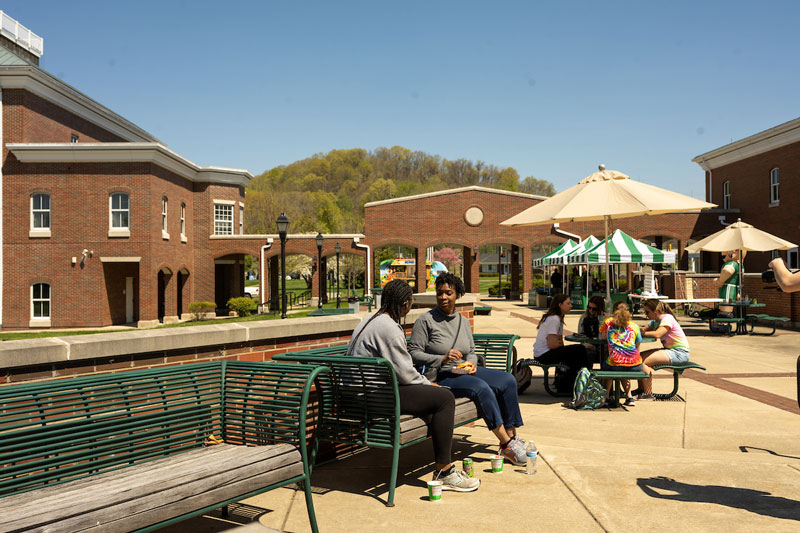 Groups of students sit on benches and outdoor tables on a patio at Ohio University’s Southern campus.