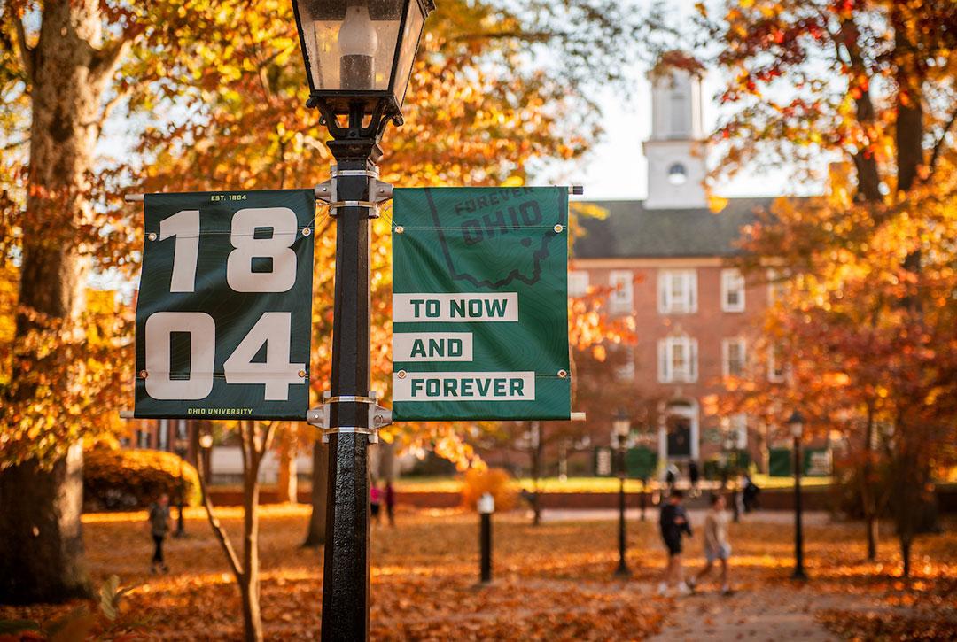 Ohio University branded banners fly on College Green, surrounded by fall foliage